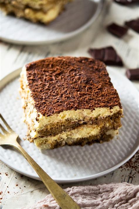 A close up shot of a square of easy Tiramisu on a white plate with a gold fork Authentic ...