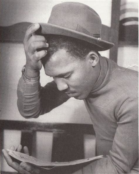 a black and white photo of a man in a hat reading a book while leaning on a chair