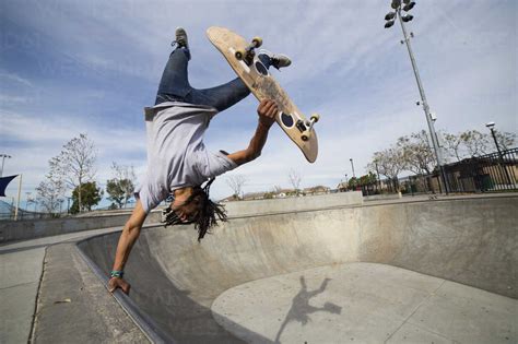 Young man doing skateboard trick upside down on edge of skateboard park ...