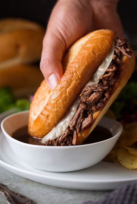 a hand is holding a sandwich over a bowl of beef and potato chips on a ...