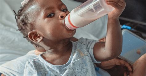 Adorable black baby sitting on bed and drinking milk from bottle · Free ...