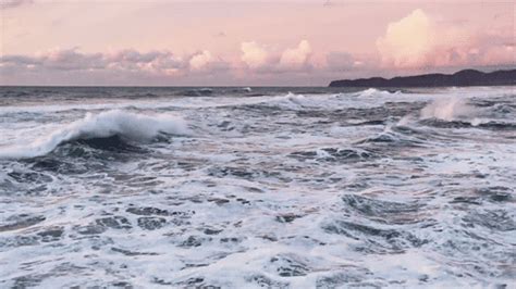 the waves are crashing on the beach in the evening time with pink sky and clouds