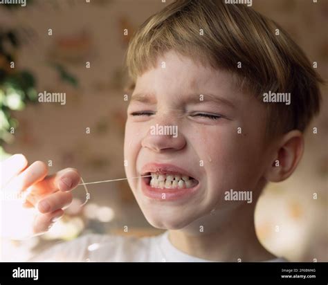 little kid with tears on his face close-up. boy tries to pull out his baby tooth with thread ...