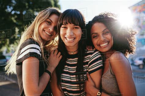 Three beautiful smiling young women friends standing together. Multi ethnic group of women ...