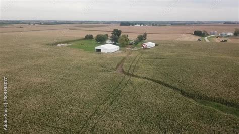 Aerial drone view in rural Iowa; flying away from a farm with barns and over green corn fields ...