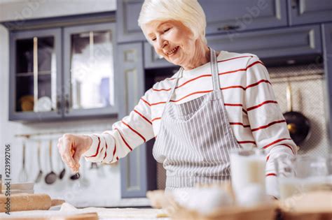 Positive grandma. Cheerful enthusiastic grandmother cooking in the modern kitchen and smiling ...