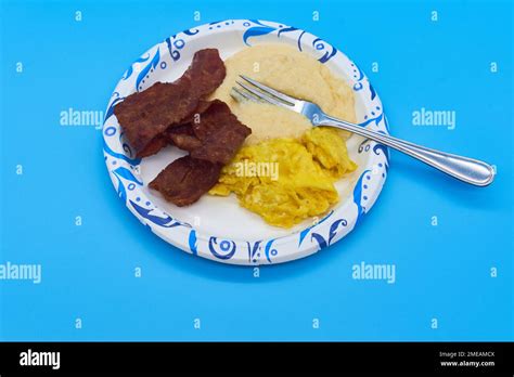 breakfast turkey bacon grits and scrambled eggs on paper plate and light blue background Stock ...
