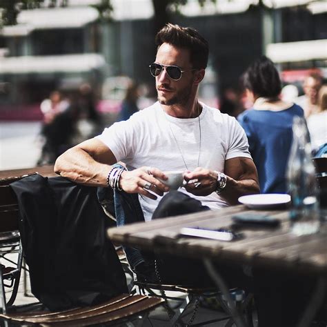 a man sitting at an outdoor table with his cell phone in his hand and other people walking by