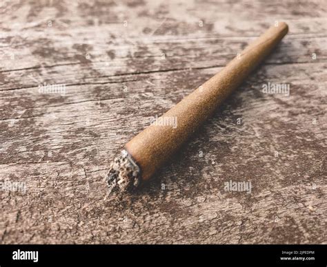 Detail of a lit marijuana or weed joint pictured on a brown wooden ...