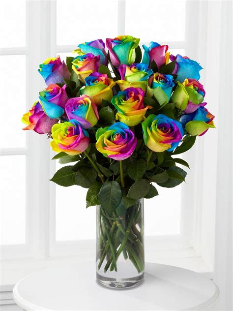 a vase filled with multi colored roses on top of a white table next to a window