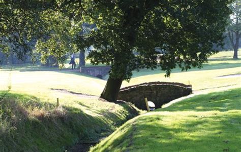 an old stone bridge over a small stream in the middle of a grassy field ...