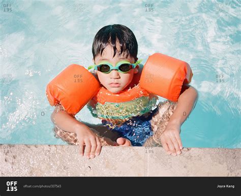 Little boy wearing floaties on the edge of a pool stock photo - OFFSET