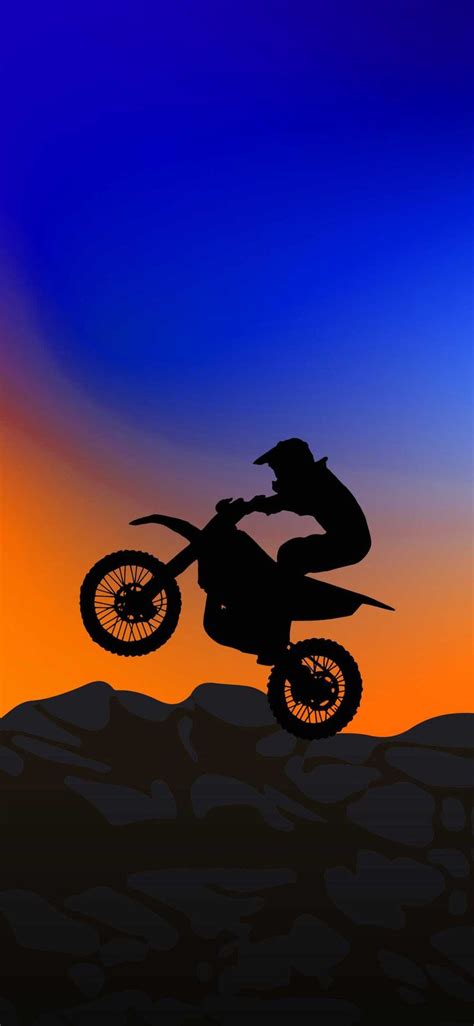 a person on a dirt bike doing a trick in the air at sunset or sunrise