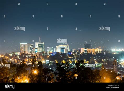 A wide view of Kigali city skyline lit up at night, under a deep blue evening sky with the glow ...