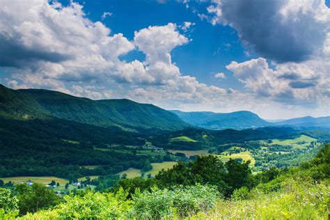 a scenic view of mountains and valleys under a blue sky with white clouds in the distance