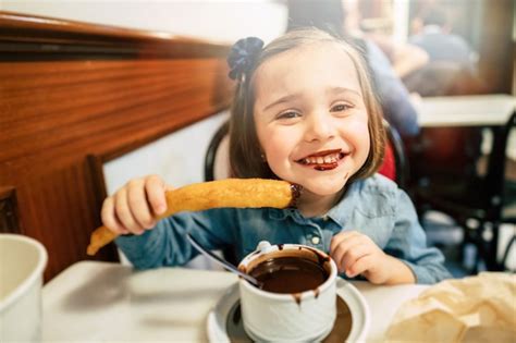 Premium Photo | Kid eating churros and chocolate