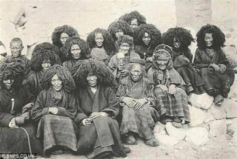 a group of women sitting next to each other in front of a stone wall ...