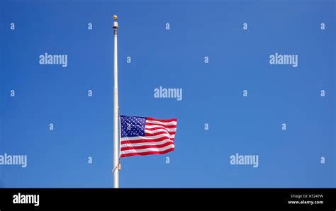 American flag flying at half mast aka half staff against a clear blue ...