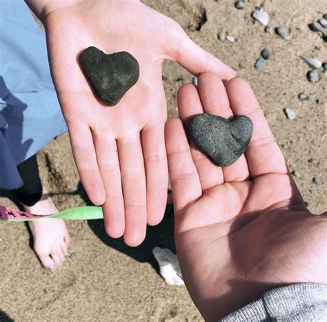 two people holding rocks in their hands on the beach, one is wearing a ...