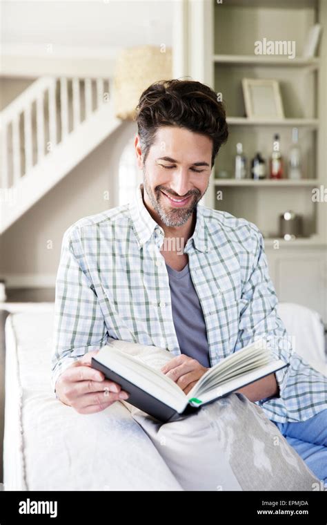 Mature man sitting on sofa, reading book Stock Photo - Alamy