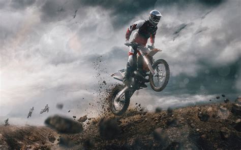 a person on a dirt bike in the air over some rocks and grass with clouds behind them