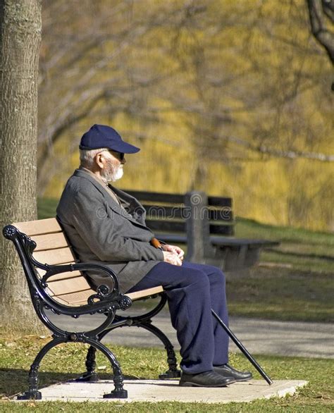 an old man sitting on a bench in the park wearing a hat and blue pants