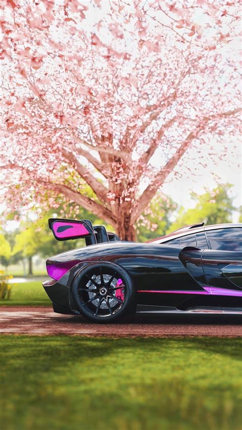 a black sports car parked in front of a tree with pink flowers on the ...