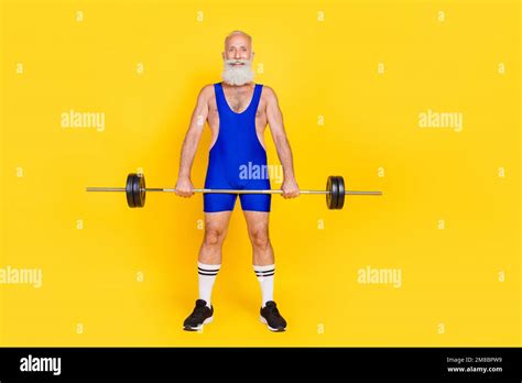 Photo of positive sportive retired guy wear blue overall pumping arms holding barbell empty ...