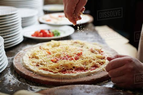 Chef sprinkling grated cheese on pizza top - Stock Photo - Dissolve