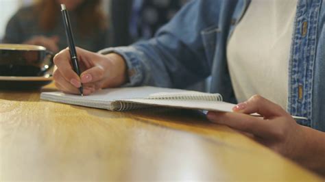 Woman writing with a pen in daily planner. Female hands writing in notebook. Side view. Slow ...