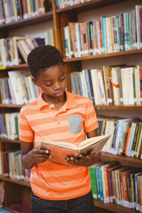 Cute little boy reading book in the library Stock Photo by Wavebreakmedia