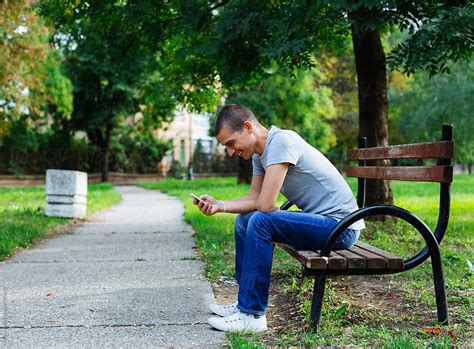 "Young Man Sitting On The Park Bench And Checking Phone" by Stocksy Contributor "Mosuno" - Stocksy