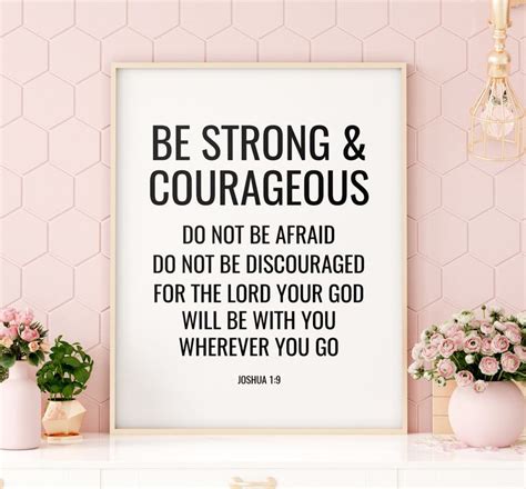 a white framed poster with the words be strong and courageous on it next to some pink flowers