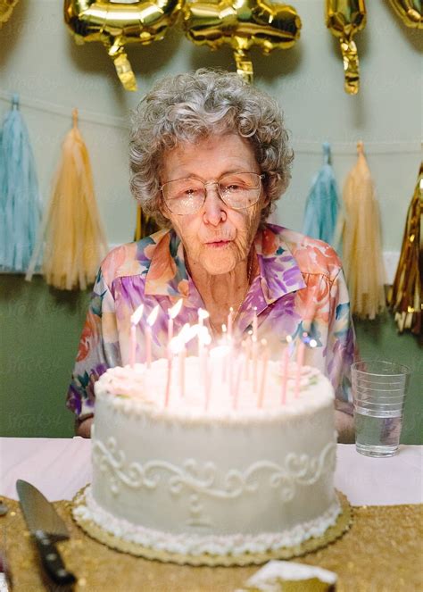 "Elderly Woman Blowing Out Birthday Candles On Cake" by Stocksy Contributor "Cameron Zegers ...