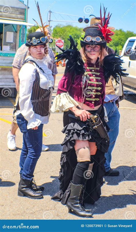 Two Women Dressed in Steampunk Costumes with Hats and Goggles Outdoors with Buildings a Truck ...