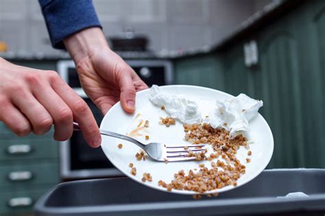 Close up of a person throwing from a plate the leftover of buckwheat to the trash bin. Scraping ...