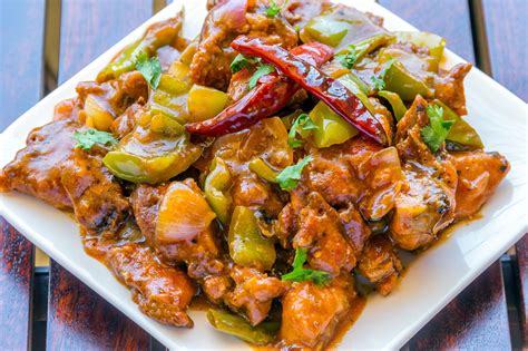 a white plate topped with meat covered in peppers and sauce on top of a wooden table