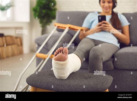 Woman with broken leg in plaster cast sitting on couch at home with mobile in hands Stock Photo ...