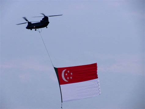 a helicopter is flying with a flag in front of a large red and white flag