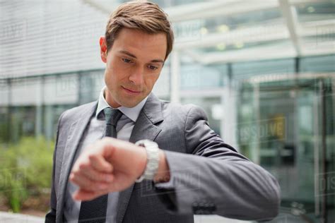 Businessman looking at watch outside office building - Stock Photo - Dissolve