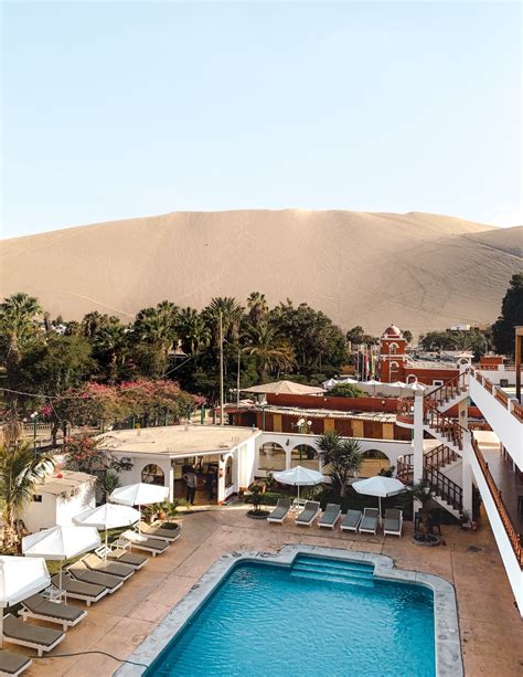 an outdoor swimming pool surrounded by lounge chairs and palm trees in front of a sand dune