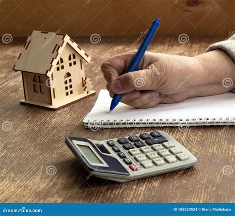 A Small Wooden House, a Calculator, a Notebook and a Pencil in Hand ...