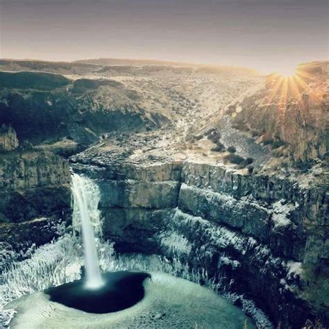 an aerial view of a waterfall in the middle of a canyon with snow on it