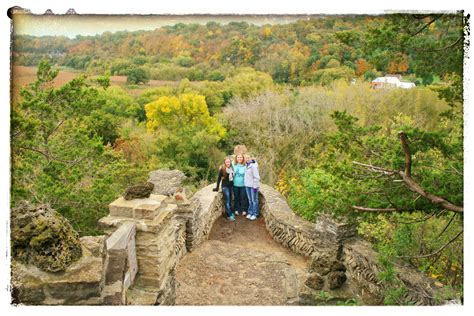 two people are standing on a stone bridge in the middle of a wooded area with trees