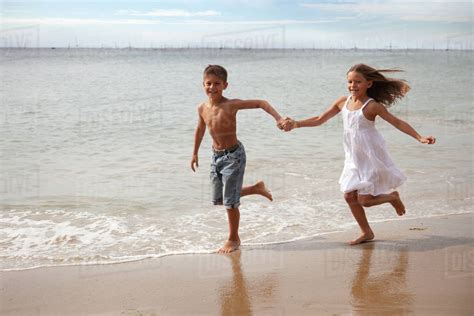 Boy and girl running along beach holding hands - Stock Photo - Dissolve