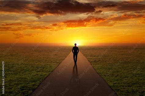 Man walking alone on a road towards the sunset Stock Photo | Adobe Stock