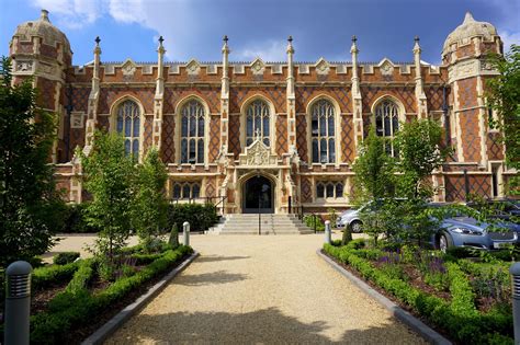 a large brick building with many windows and plants on the front lawn, surrounded by greenery