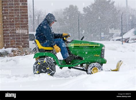 John Deere riding lawn mower fitted with a snow plow removing snow from ...