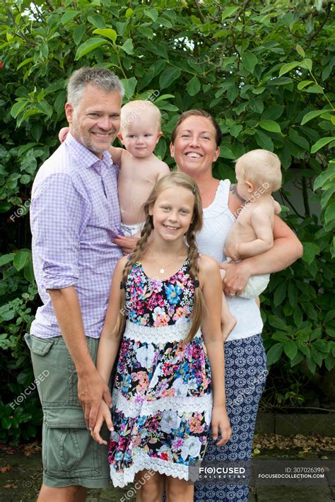 Portrait of happy family with three children standing together outdoors and smiling at camera ...