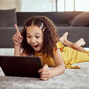 Full length adorable little mixed race child using digital tablet and thinking at home. One ...